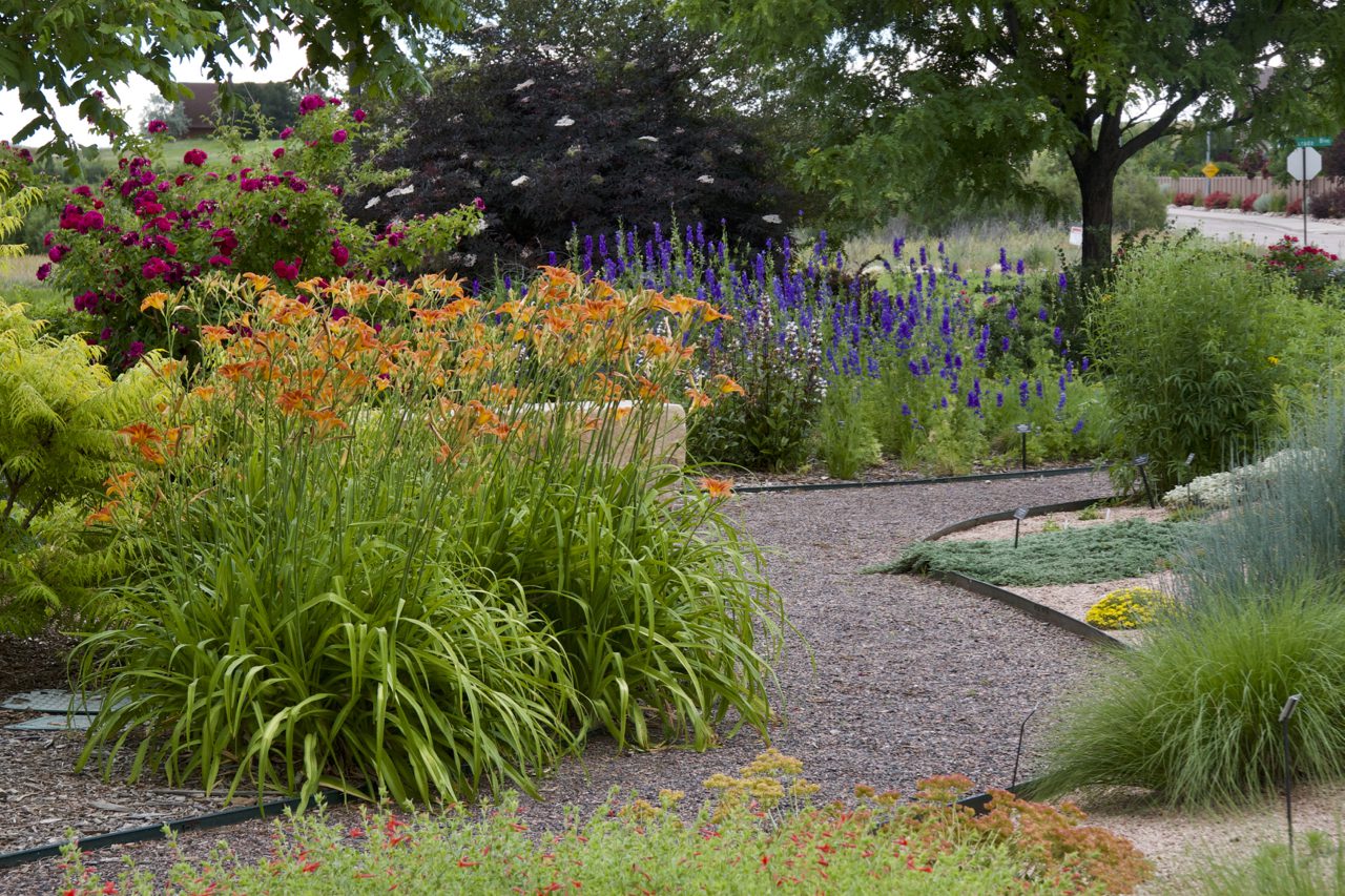 A gravel path weaves between orange, red and purple flowers and green bushes.