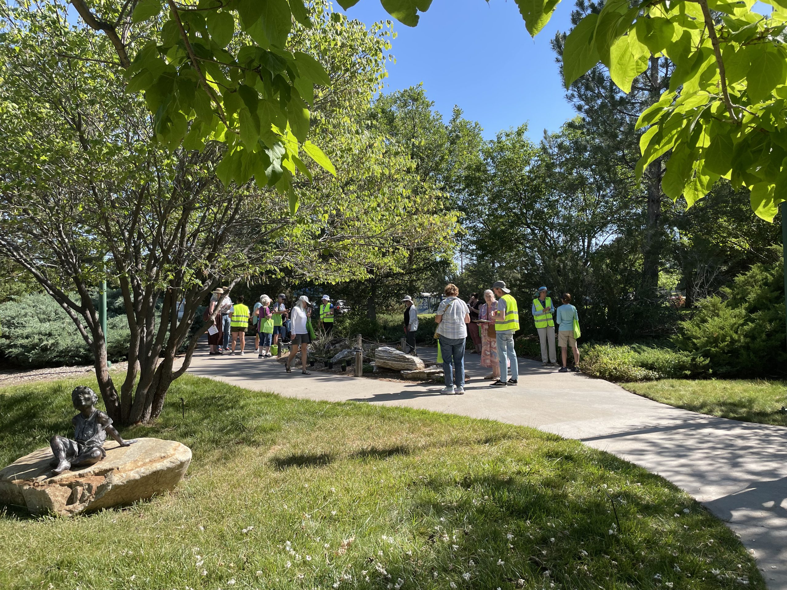 Event attendees stand on a garden pathway surrounded by green trees and grass.