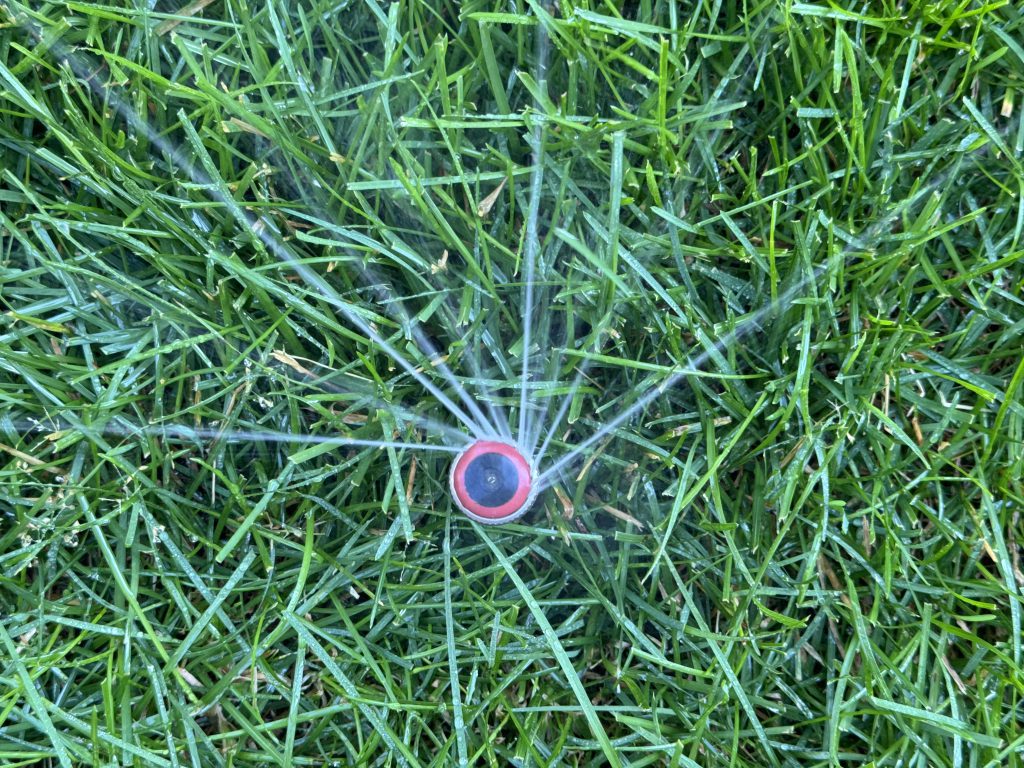 Overhead of a rotary nozzle spraying water on green grass.