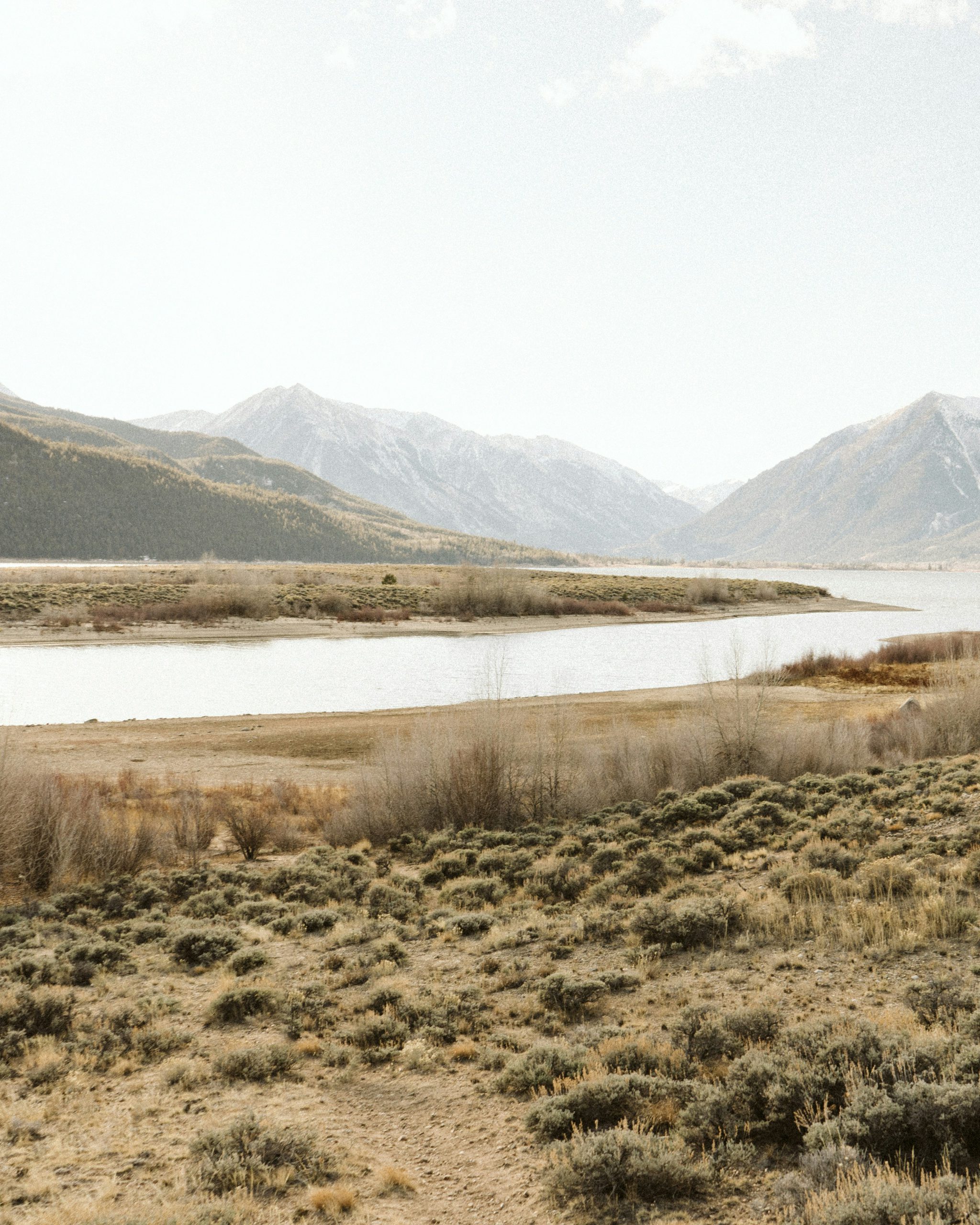 Dry landscape with bushes and shrubs, a large river in the middle ground, and large mountains in the background.