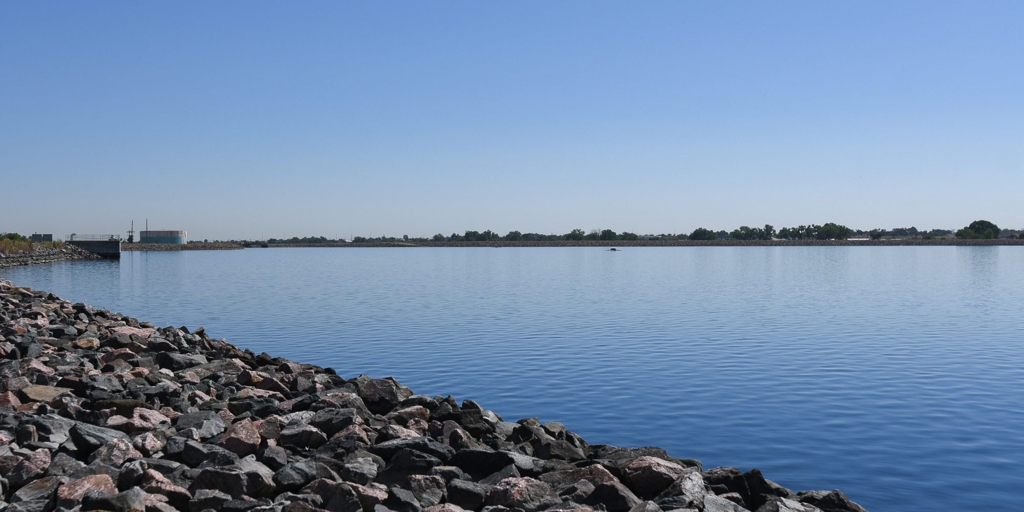 Blue body of water surrounded by large rocks. There is a bright blue sky with no clouds in the background.