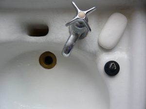 A cracked white sink basin with a turn spout, brass drain pipe and white bar of soap.