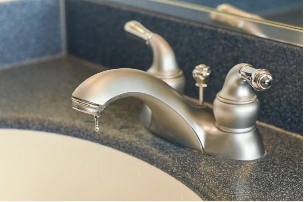 Close-up silver bathroom faucet with a small water drip from the spout